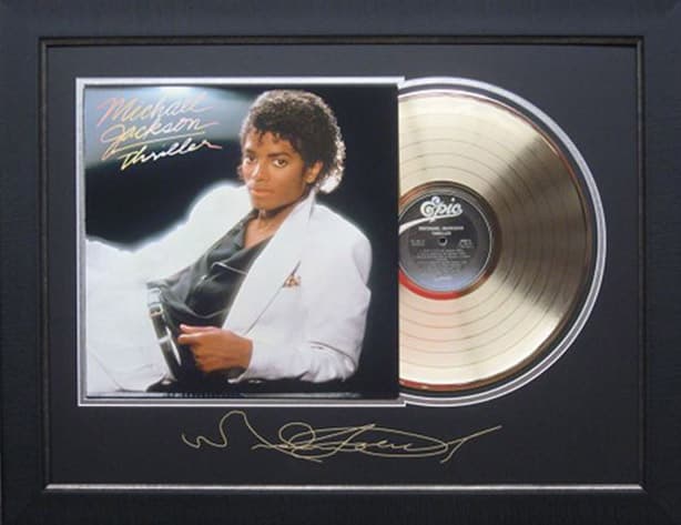 Framed gold record displayed beside the Michael Jackson Thriller album cover with a laser-reproduced signature, offered as a charity auction lot